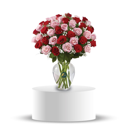 A bouquet of pink and red roses arranged in a clear glass vase
